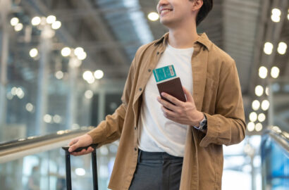 Asian young man passenger walking in airport terminal to boarding gate. Attractive handsome male tourist feeling happy and excited for going travel abroad by airplane alone for holiday vacation trip.